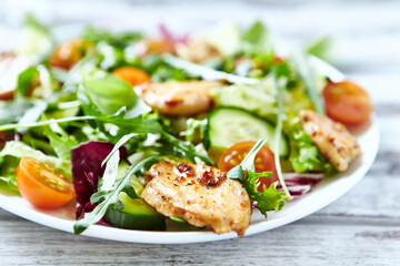 Salad with Chicken Breast, Cherry Tomatoes, Cucumber, Rocket and fresh Basil. Bright wooden background. Close up.