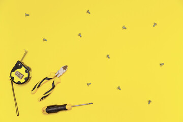 A flatlay with a set of bench tools, screwdriver, cutting pliers, tape measure and screws on yellow Illuminating background. Colors of the 2021 year.