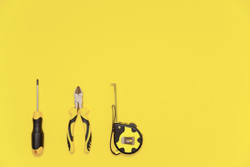 A flatlay with a set of bench tools, screwdriver, cutting pliers and tape measure on yellow Illuminating background. Colors of the 2021 year.