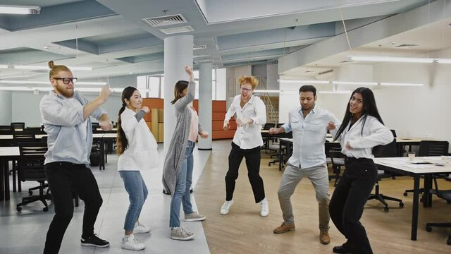 Young team of multiracial diverse colleagues are smiling and dancing rejoicing about developing of a new business project