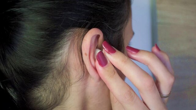 Attractive young girl putting in her ear white wireless earphones, close up