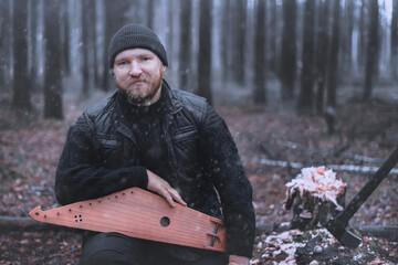 Portrait of a frendly bearded man with the traditional Finnish musical instrument Kantele in the...