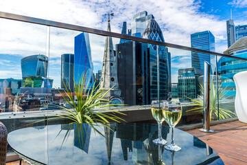 LONDON, UK; Sep 2020; two glasses of wine on the foreground and blurry aerial view of skyscrapers of the world famous bank district of central London at sunset