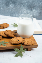 A glass cup of milk with chocolate cookies on a wooden cutting board