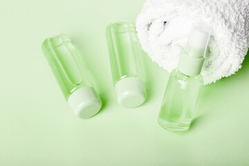 Three bottles of tonic or lotion and white towel on green background. Freshness and body care. Travel set of face care cosmetic. Three  bottles of hand sanitizer. Liquid soap and sanitizer for hands