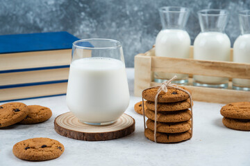 A glass cup of milk with chocolate cookies on a wooden board