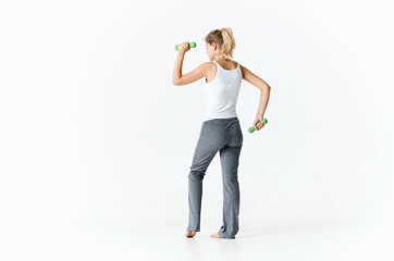 woman goes in for sports with dumbbells in a bright room and gray pants