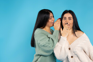 Two caucasian sisters on blue background. Discussion about amazing news with bright smiles.