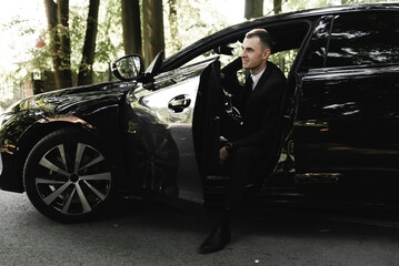 young businessman is sitting in an expensive car and looking at the camera. the groom is driving. business man. successful guy. rich man.