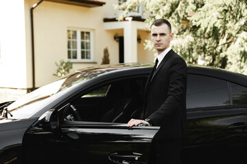 young successful businessman stands in front of his expensive car. rich young guy. rich man. car on the background of a businessman. groom with car on wedding day