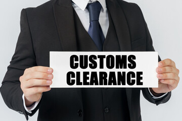 A businessman holds a sign in his hands which says CUSTOMS CLEARANCE