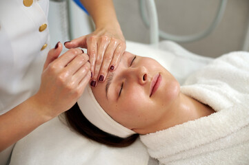 A happy woman enjoying while cosmetologist making a lifting facial massage