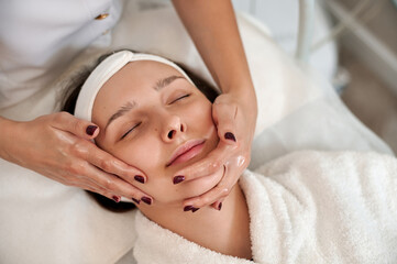 Cosmetologist making lifting facial massage for woman's face and neck. Closeup