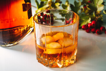 glass of whiskey with ice next to a bottle and a branch of viburnum