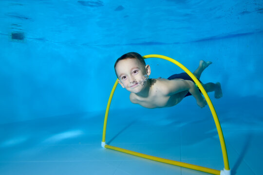 A little boy dives under the water in a children's pool. It floats through the Hoop. Active happy child. Healthy lifestyle. Swimming lessons under the water. A family sport - Powered by Adobe