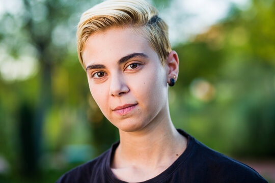 Young woman beauty Tomboy lifestyle with blonde short hair posing in casual clothes in a park in Spain.
Jeans and t-shirt showing armes, gender education and non binary teen.