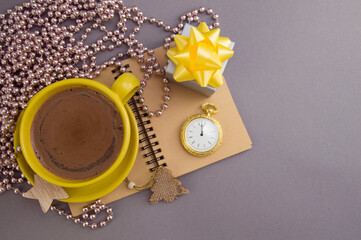 Winter flat lay. Blank open notebook, yellow cup with coffee, New Year's pink beads, gift box with a yellow bow.