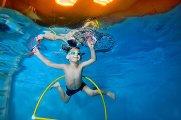 Portrait of a little boy in class underwater in a children's pool. He swims through the Hoop, pulls...