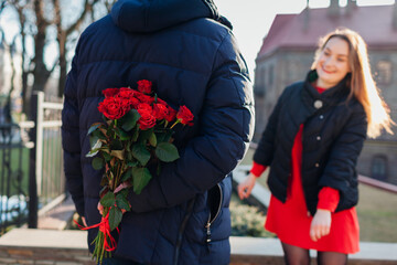 Valentines day surprise. Man hiding bouquet of roses flowers from girlfriend behind his back on date outdoors.