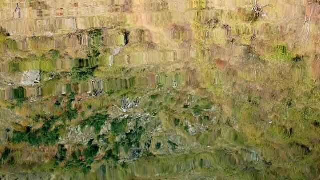 Reflection of mountain side covered with dry yellow grass in mountain lake. Sunny autumnn wamr day with nice weather.