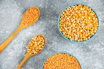 Two bowls of corn kernels and red lentil on marble surface