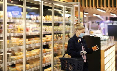 Woman choosing frozen food from a supermarket freeze.Supermarket shopping, face mask