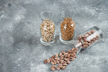 Three glasses of jar with unprepared beans on a gray background