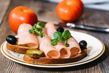 piece of bread with smoked ham, cucumbers, olives and tomatoes on a wooden table