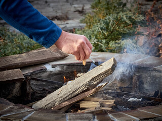 Man touching wooden log while making bonfire near stones