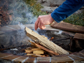 Man touching wooden log while making bonfire near stones