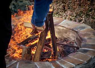 Man touching wooden log while making bonfire near stones