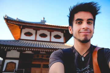 Handsome young traveler with traditional japanese temple behind at Miyajima, Japan