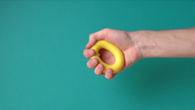 Hand unsuccessfully tries squeeze yellow hand expander many time blue background