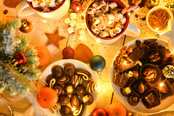 sweet food top view background for merry christmas or new year holiday decoration with night illumination - chocolate candies, tangerines, cookies, marshmallow and cocoa latte on white wood