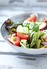 Salad with radish, green olives, tomatoes, cucumber and fresh basil. Bright wooden background. Close up. 