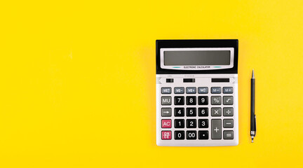 Large silver calculator with gray and black buttons and black pen on a yellow background. Conceptual photo of calculations, accounting, computing, profit, loss, tax. Business card with copy space