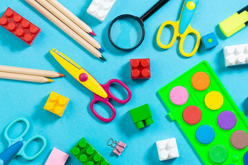 Bright stationery supplies and plastic constructor bricks on bright blue background top view. Preschool education concept.