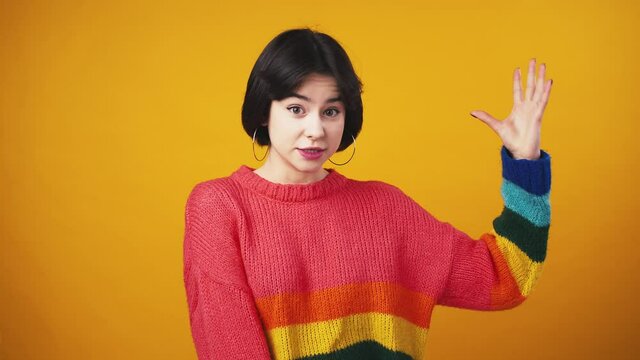 Cute woman wearing red sweater with rainbow sleeves showing bellissimo gesture and smiling to camera, orange background