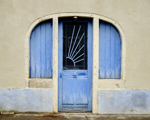 Old vintage 19th century wood blue door, with large sun metal window protection, framed two arched shuttered windows