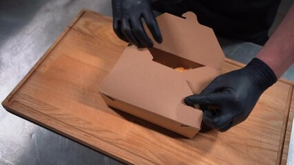closeup of chef cook hand in medical gloves packing food in cardboard container