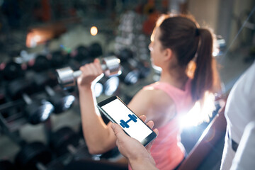 young female has personal online workout or exercising with dumbbells in gym
