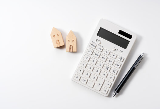 A model of a house, a calculator and a pen on a white background