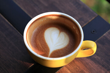 Hot coffee with heart shape latte art topping on yellow cup