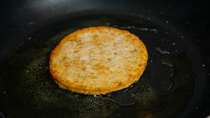 Closeup shot of a chicken burger patty in an oily frying pan.
