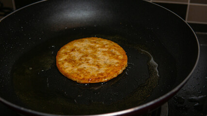 Closeup shot of a chicken burger patty in an oily frying pan.