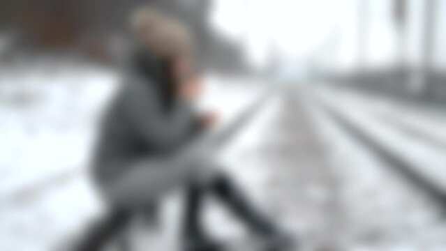 Blurred background. One girl sits on rails with mug of tea thermos