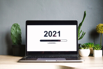 Loading the new year 2021 on a laptop screen with succulents and decorative plants on a wooden table with grey background. Minimalist festive concept