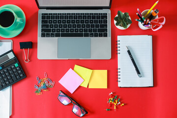 Flat lay top view of stylish home office with laptop, a cup of coffee, succulent and accessories isolated on red background