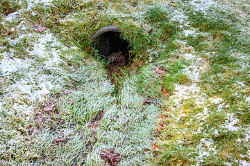 Frosty flood control, grass covered rainwater drainage ditch with metal culvert pipe
