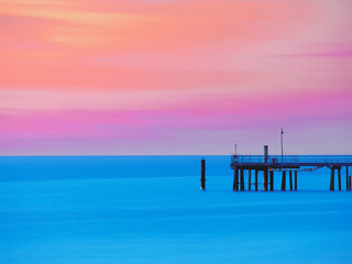 Fototapeta na wymiar Sunset at Glenelg beach and jetty with twilight in purple, yellow, and orange colours. 